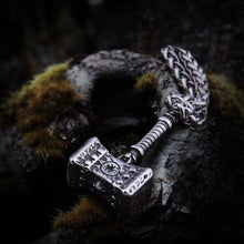 Rugged silver Viking Thor's Hammer pendant with intricate chain, resting on mossy wood.