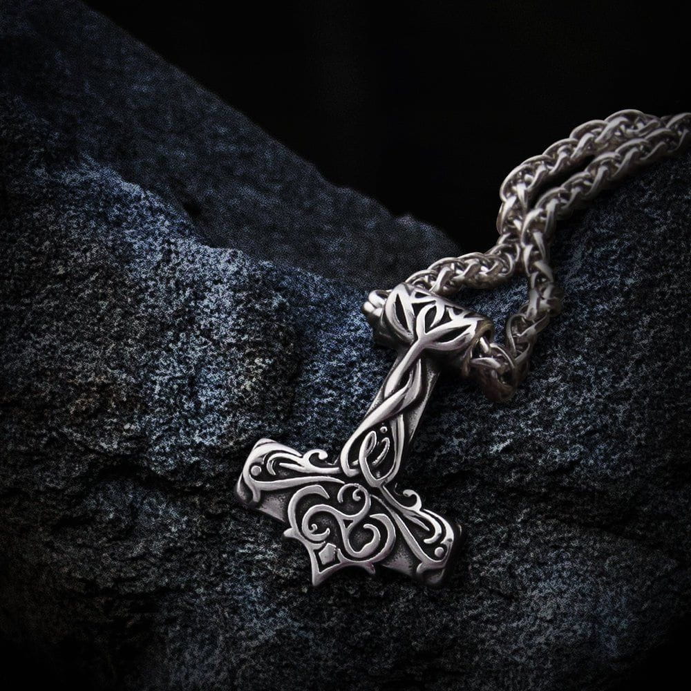 Silver Viking Thor's Hammer necklace with intricate Triskelion scrollwork design on a dark, textured surface.