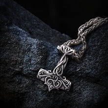 Silver Viking Thor's Hammer necklace with intricate Triskelion scrollwork design on a dark, textured surface.