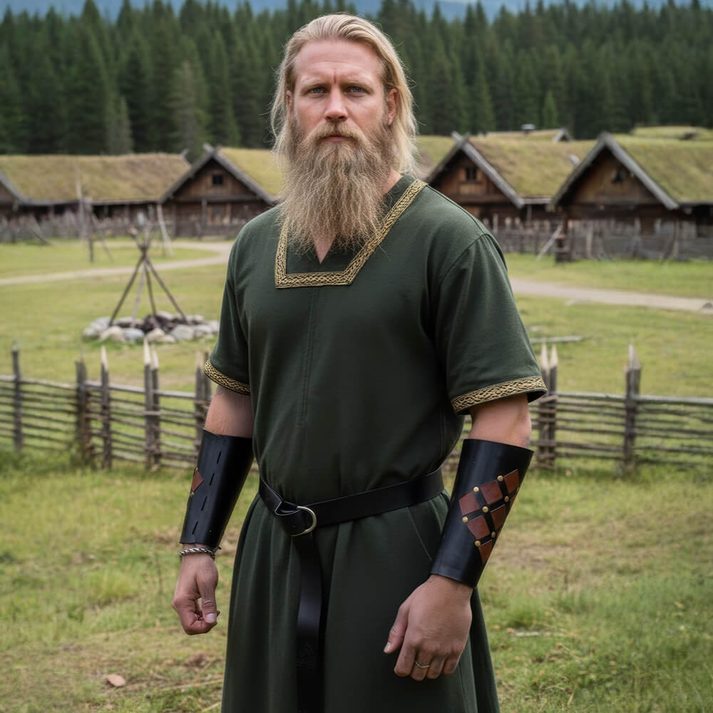 Bearded man in a green nobles' Viking tunic stands in a village with wooden huts and forest in the background.