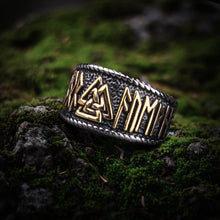 Viking Valknut ring with gold Futhark runes on a dark silver band, resting on moss.