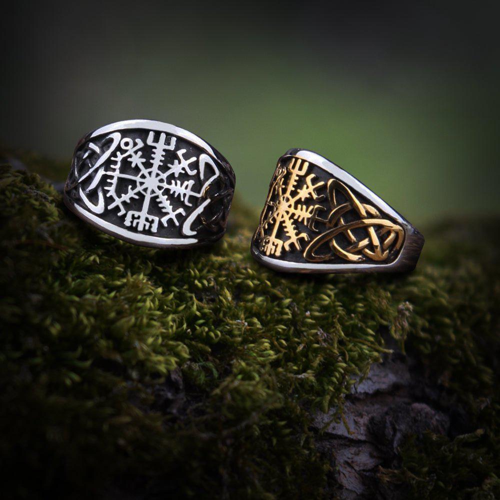 Two Viking Vegvisir compass rings, one silver, one gold and silver, with bold knotwork on mossy wood.