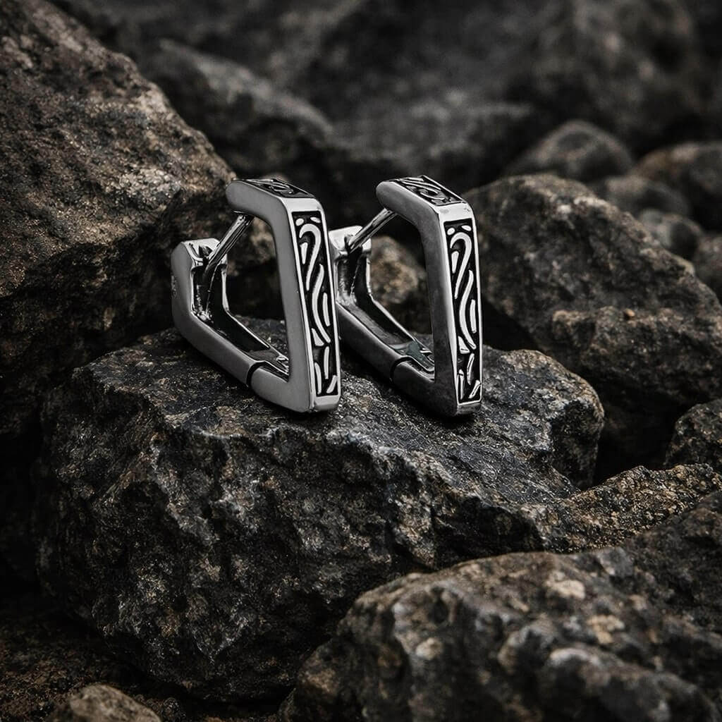 Viking silver angular hoop earrings with intricate black knotwork design on dark rocks.