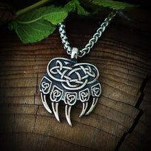 Viking silver bear claw necklace with intricate Celtic knotwork design on a wooden surface.