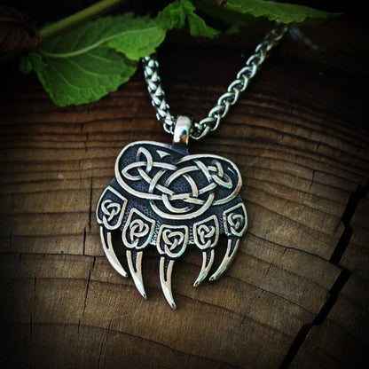 Viking silver bear claw necklace with intricate Celtic knotwork design on a wooden surface.
