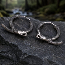 Viking coiled serpent hoop earrings with an antiqued silver finish, resting on dark stone.