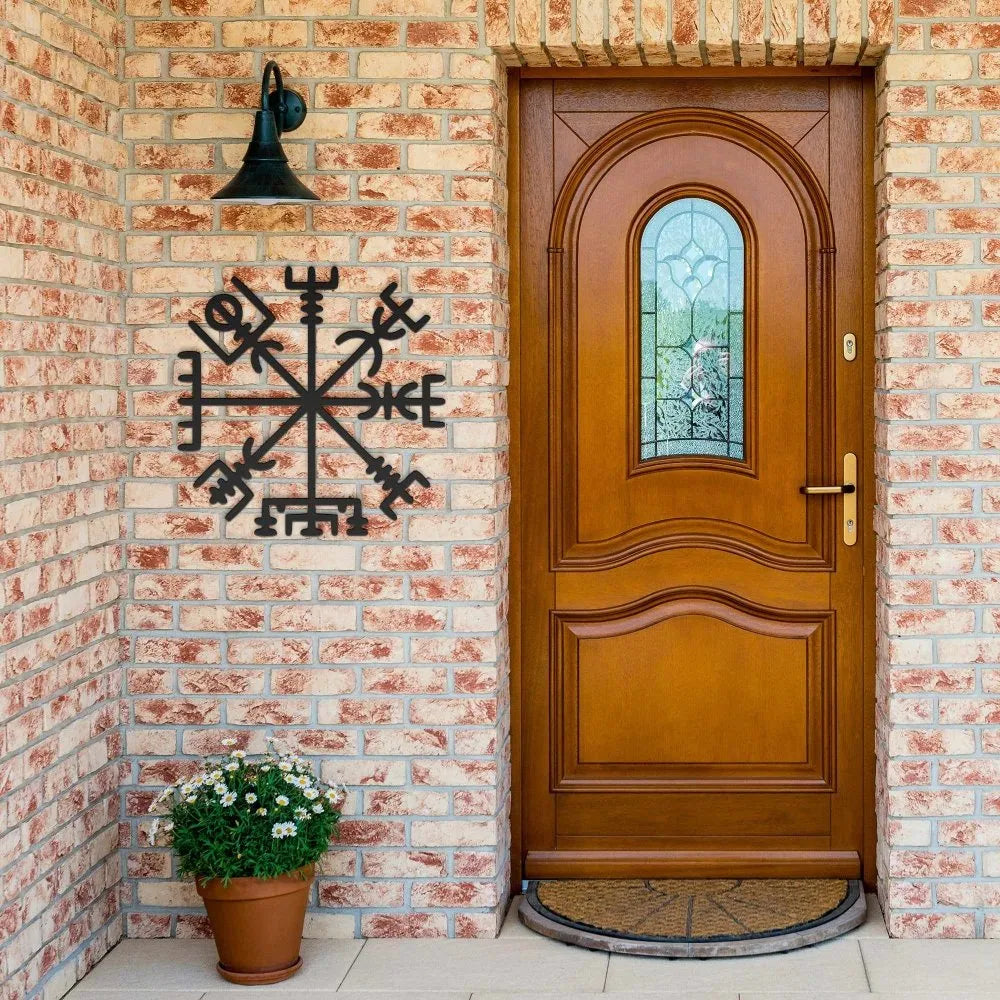Black metal Viking Vegvisir compass wall sign on a brick wall next to a wooden door.