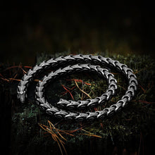Viking Jormungandr segmented steel necklace with dragon scale design on mossy wood.