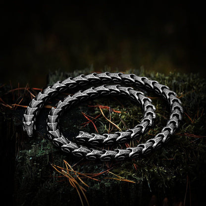 Viking Jormungandr segmented steel necklace with dragon scale design on mossy wood.
