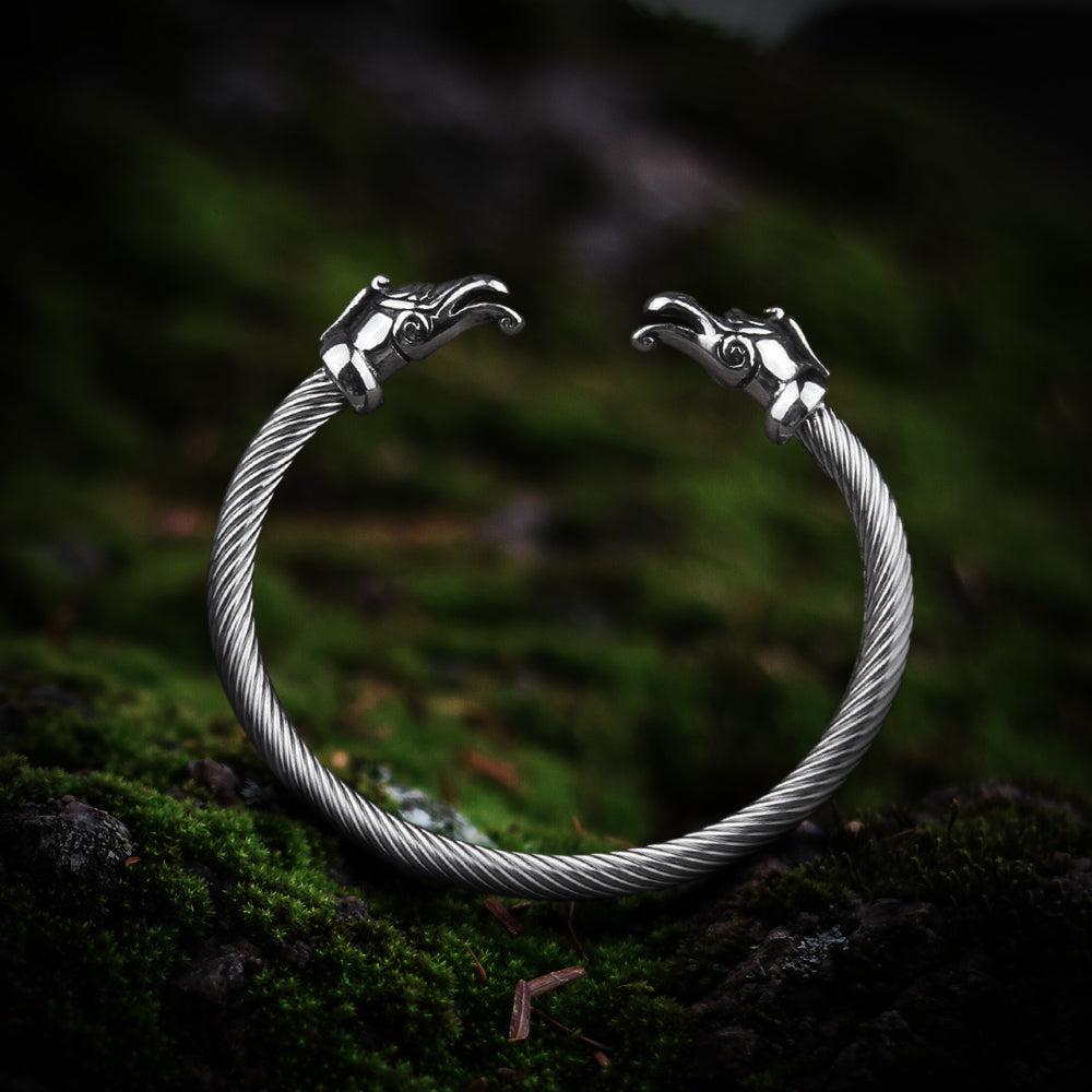 Viking silver torc arm ring with detailed dragon heads, twisted metal band, on mossy ground.