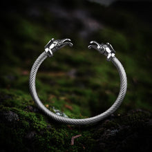 Viking silver torc arm ring with detailed dragon heads, twisted metal band, on mossy ground.