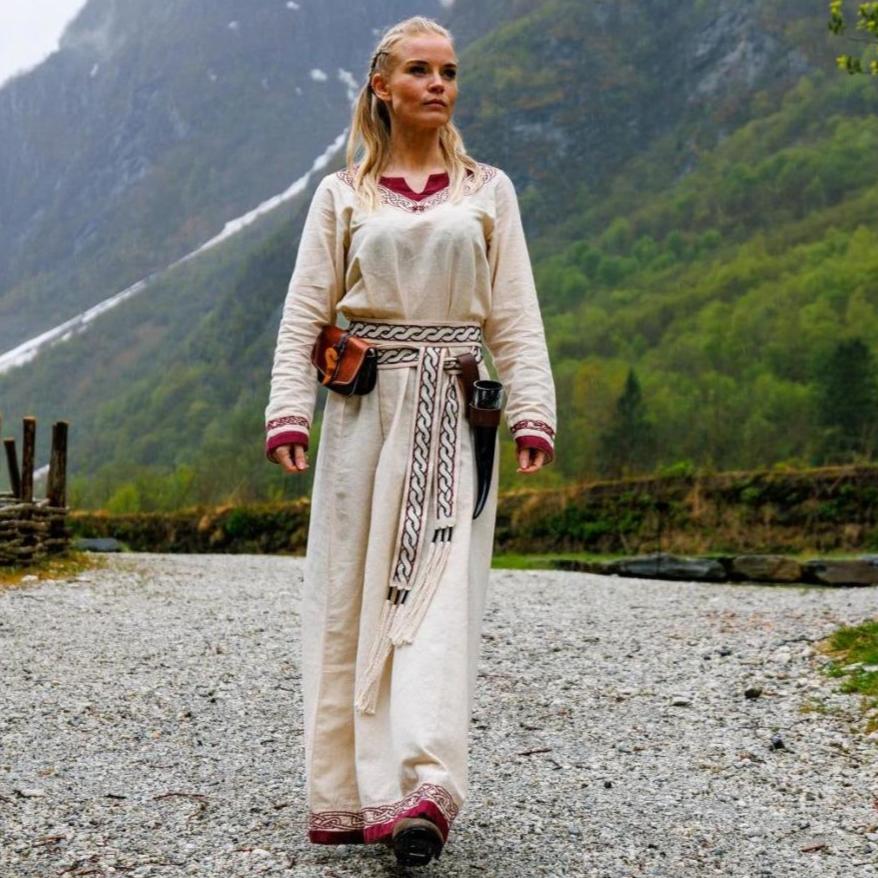 Viking dress in natural linen with red trim, embroidered belt, and leather pouches.