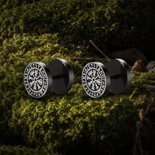 Black Viking stud earrings with white Norse Vegvisir compass symbol on mossy ground.