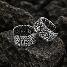 Two silver Viking Elder Futhark rune open cuff band earrings on dark rocks.