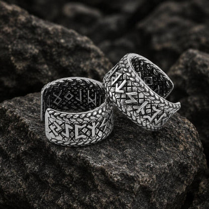 Two silver Viking Elder Futhark rune open cuff band earrings on dark rocks.