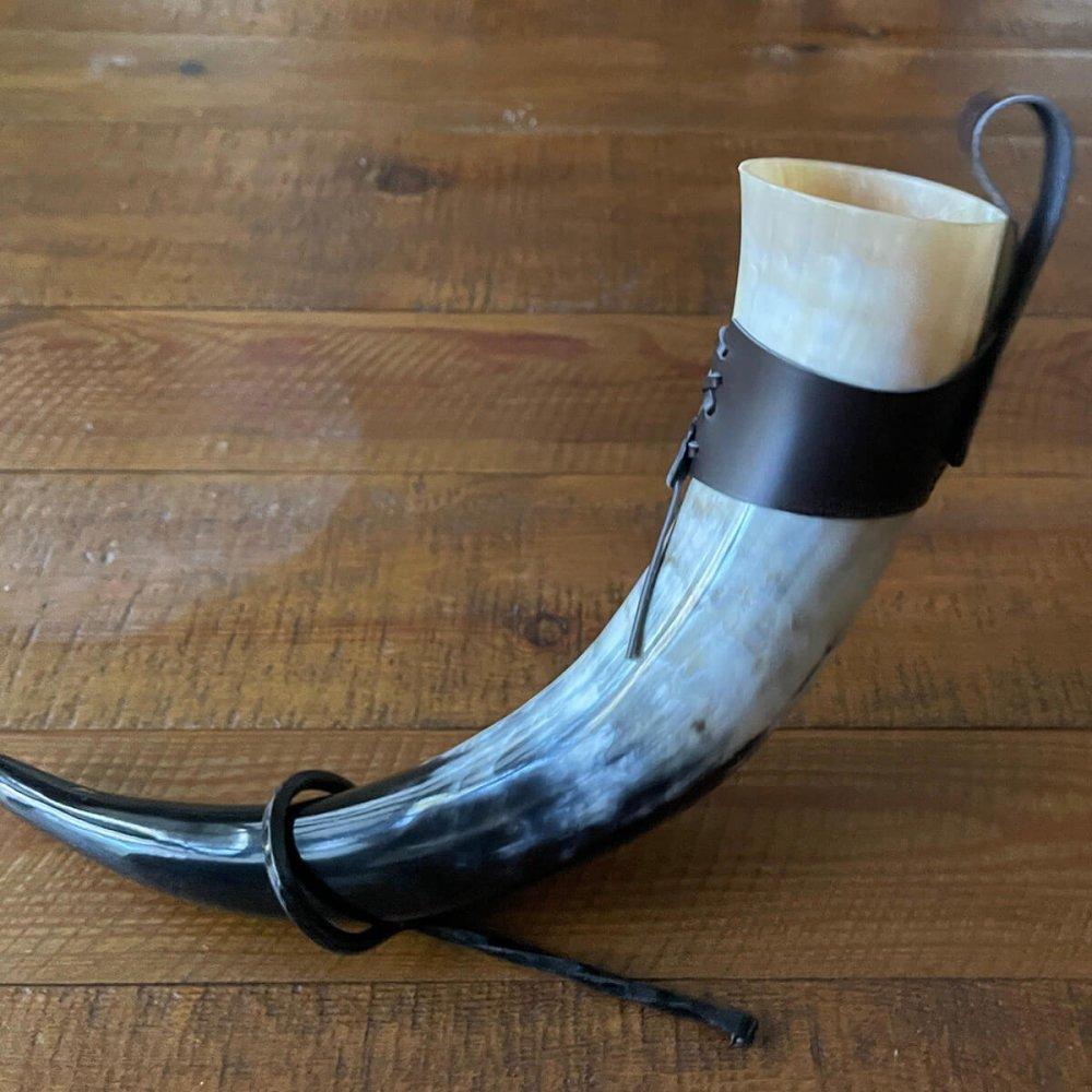 Viking drinking horn with natural black and white hues, a dark leather belt loop, and a tied leather strap.