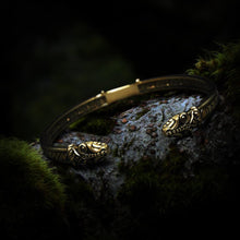 Viking Jormungandr bronze bracelet with engraved Elder Futhark runes, resting on mossy bark.