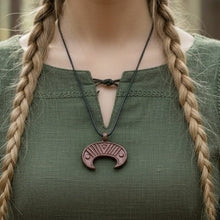Viking Luna pendant: bronze crescent moon with geometric details on a black cord, worn over a green tunic.