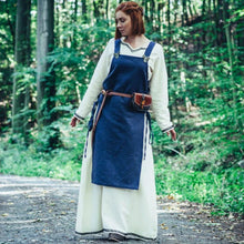 Viking woman in a cream cotton underdress and blue apron overdress with leather belt and pouch.