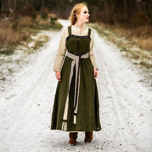 Viking woman in a green linen overdress with a beige undershirt and decorative belt, walking on a snowy path.