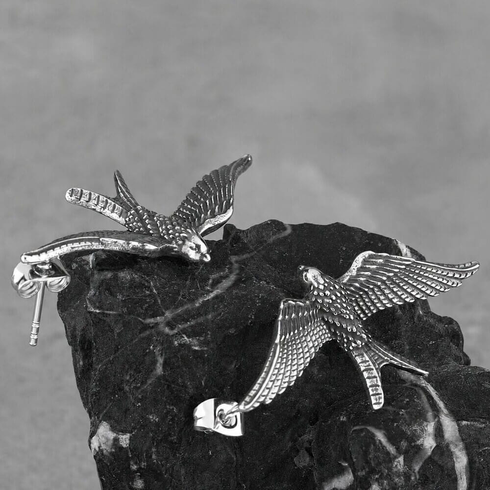 Viking silver raven wing drop earrings with detailed feathered Norse design on a dark rock.