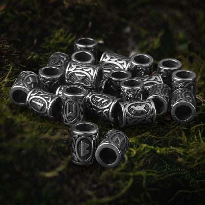 Viking Futhark rune steel beard beads, silver-toned with intricate patterns, on green moss.