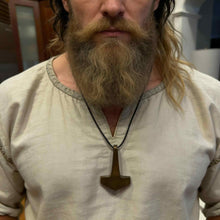 Viking Thors Hammer (Mjolnir) pendant in dark iron, worn on a black cord over a light tunic.