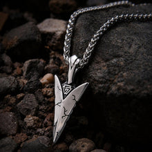 Viking Tyr arrowhead pendant necklace with Valknut design, silver-toned metal, on dark rocks.