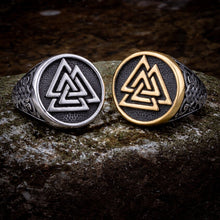 Two Viking signet rings on a rock: one silver, one with a gold Valknut Celtic knot design.