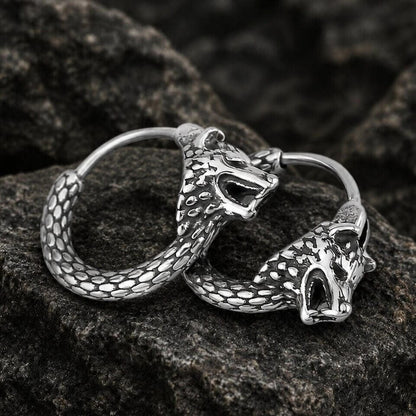 Viking silver wolf head hoop earrings with textured scales, resting on dark rocks.