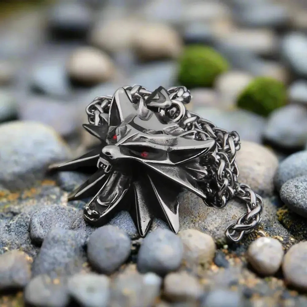 Viking darkened steel wolf head necklace with red eyes, resting on grey rocks.