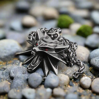 Viking darkened steel wolf head necklace with red eyes, resting on grey rocks.