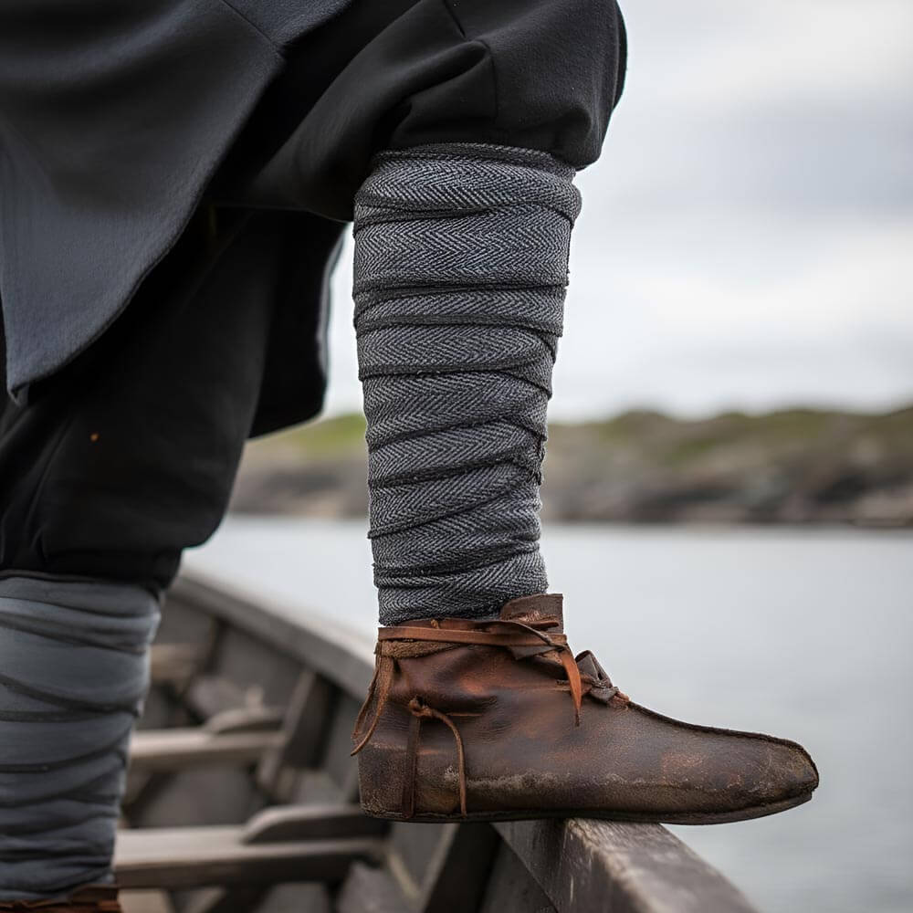 Viking grey herringbone wool leg wraps (winingas) over dark trousers, with brown leather shoes, on a boat.