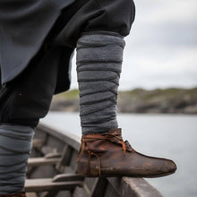 Viking grey herringbone wool leg wraps (winingas) over dark trousers, with brown leather shoes, on a boat.