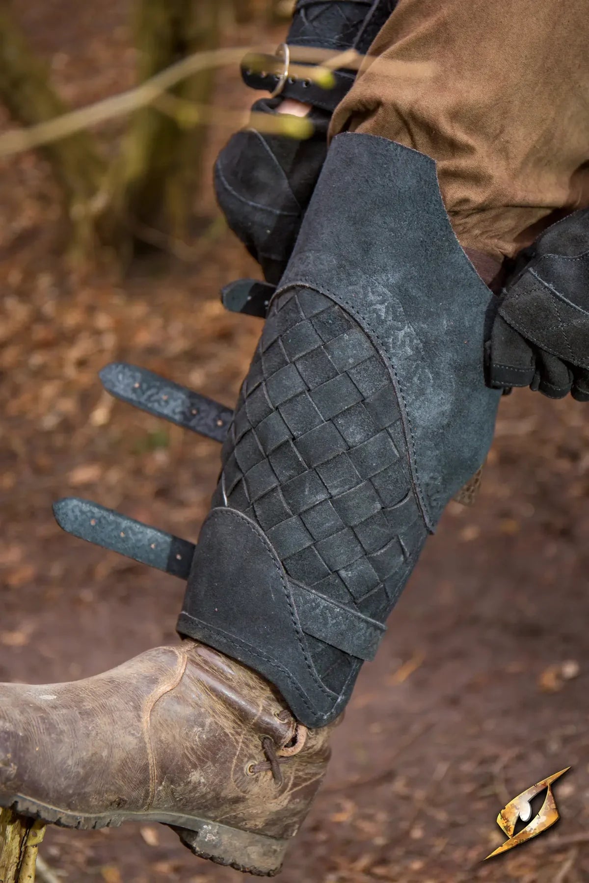 Dark gray woven leather Viking greaves with adjustable straps over a brown boot.