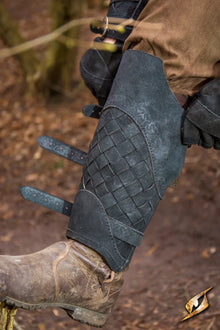 Dark gray woven leather Viking greaves with adjustable straps over a brown boot.