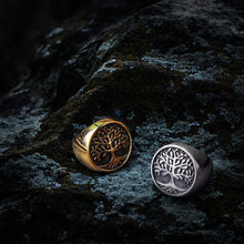Gold and silver Viking Yggdrasil Tree of Life rings on dark, textured rock.