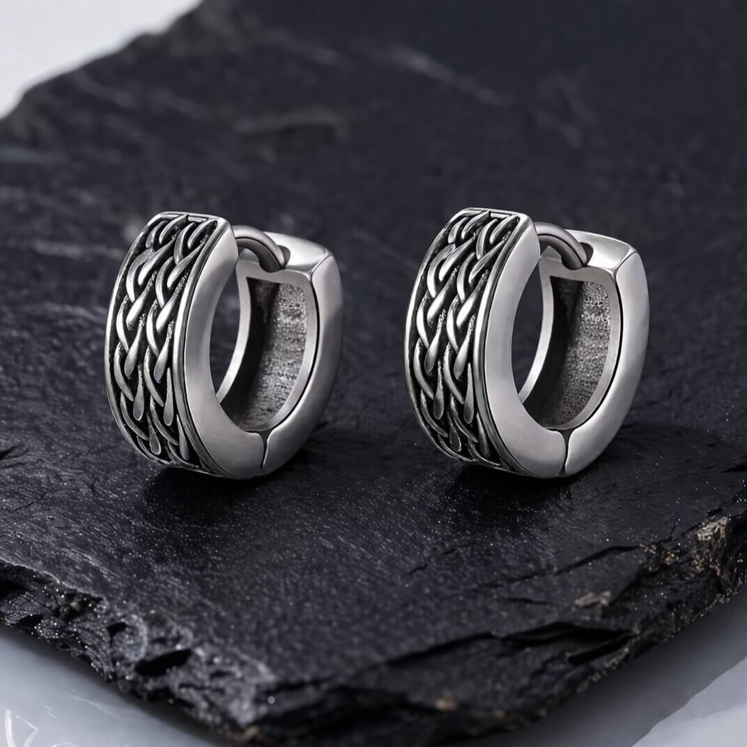 Celtic knotwork huggie hoop earrings in antiqued stainless steel with braided weave pattern displayed on dark slate