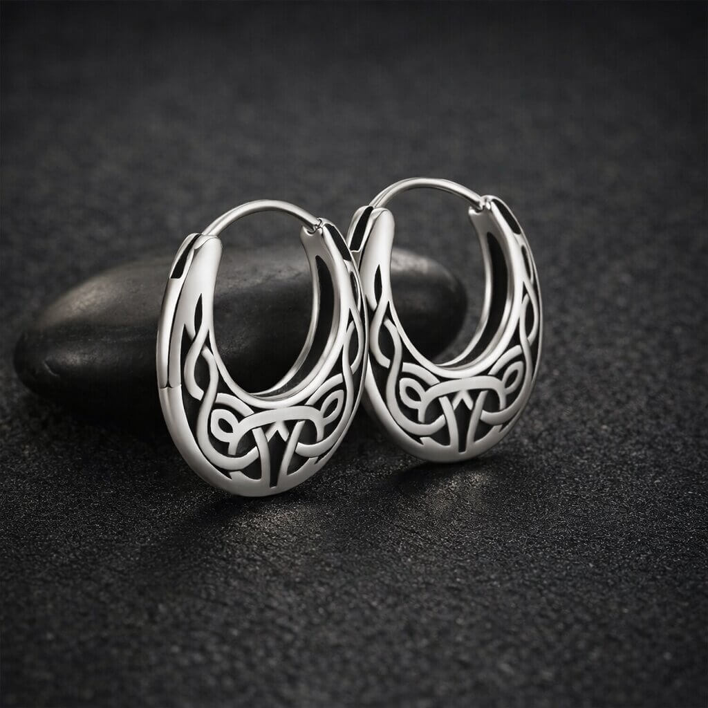 Celtic knotwork oval hoop earrings in polished stainless steel with openwork endless knot design displayed on black stone