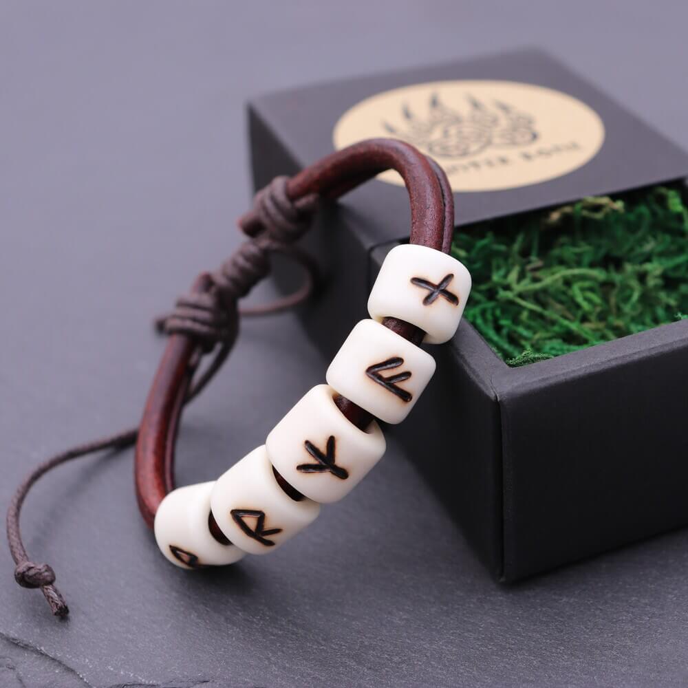 Handmade Elder Futhark rune bead leather Viking bracelet with white rune beads on a dark cord beside a black gift box.