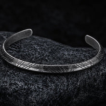 Viking arrow cuff bracelet in antiqued silver stainless steel featuring deeply engraved chevron and diagonal line pattern representing arrow fletching – adjustable open band design displayed on dark granite stone – Norse Tyr warrior symbol jewelry for men