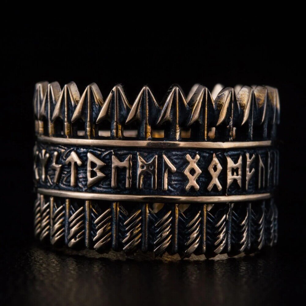 Handcrafted Viking bronze ring featuring three bands – top row of Tyr arrow symbols, center band with complete Elder Futhark runic alphabet, bottom band with diagonal chevron feather pattern – oxidized black finish with raised bronze details