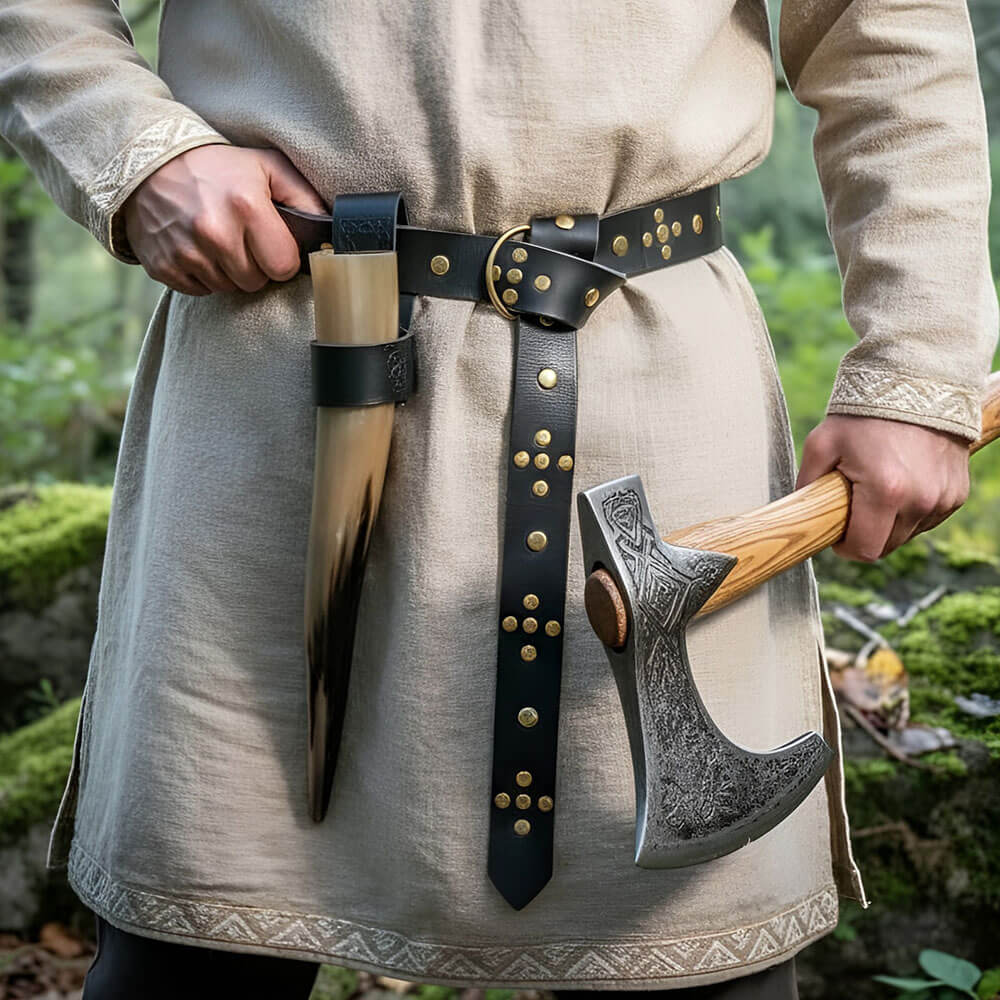 Riveted black leather Viking belt with ring loop and knotted design, worn over a beige tunic, holding a drinking horn and engraved Viking axe.