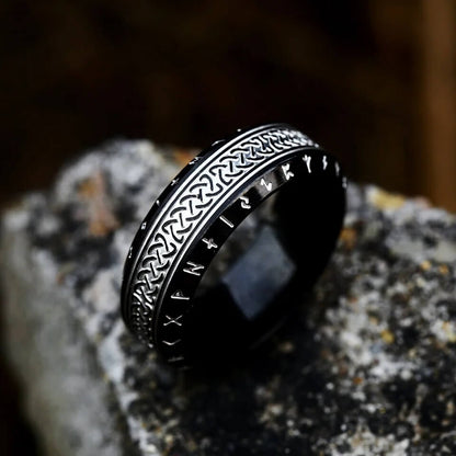 Black Rune Celtic Knot Stainless Steel Ring featuring silver Elder Futhark alphabet on edges and woven Celtic braid pattern on center band displayed on stone