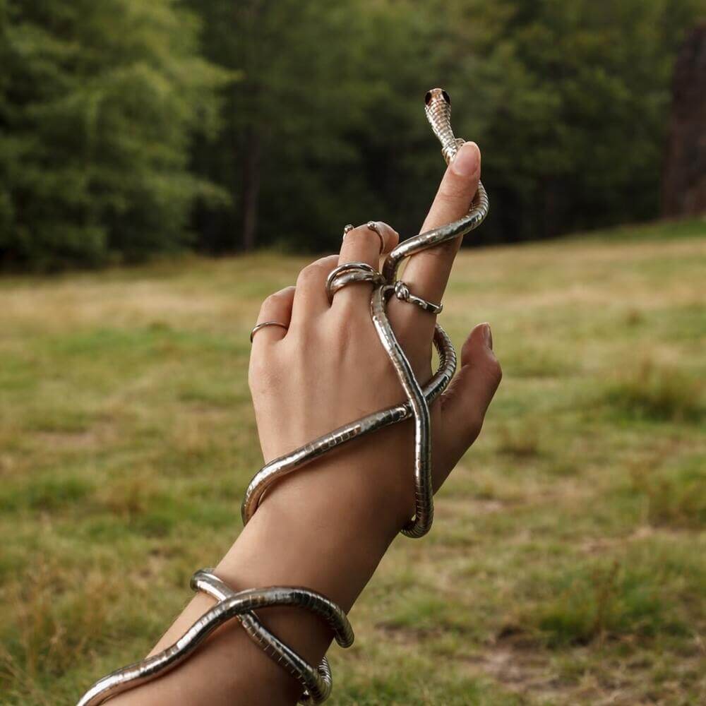 A silver serpent wrap Viking jewelry bracelet coils around a hand with rings, posed against a lush woodland setting.