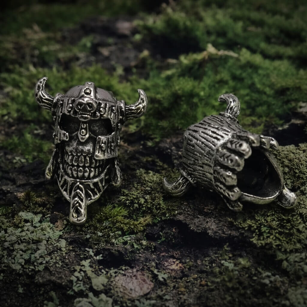 Two intricately carved Skull Viking Warrior beard beads rest on mossy ground, showcasing fierce Norse design and detail.
