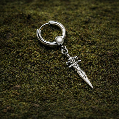 A stainless steel dagger hoop earring with ornate detailing rests on a textured bed of green moss.