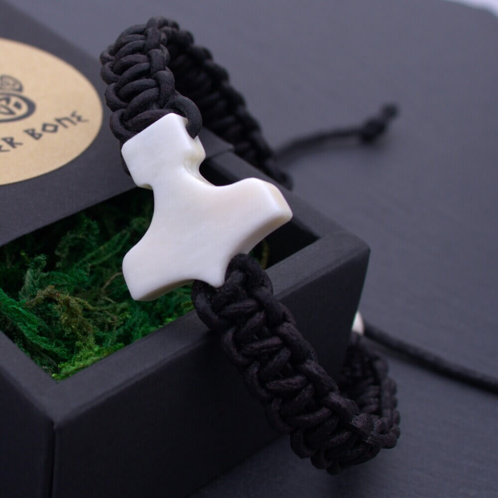 Thor’s Hammer Bone-White Pendant Braid Bracelet displayed on a black gift box filled with green moss.