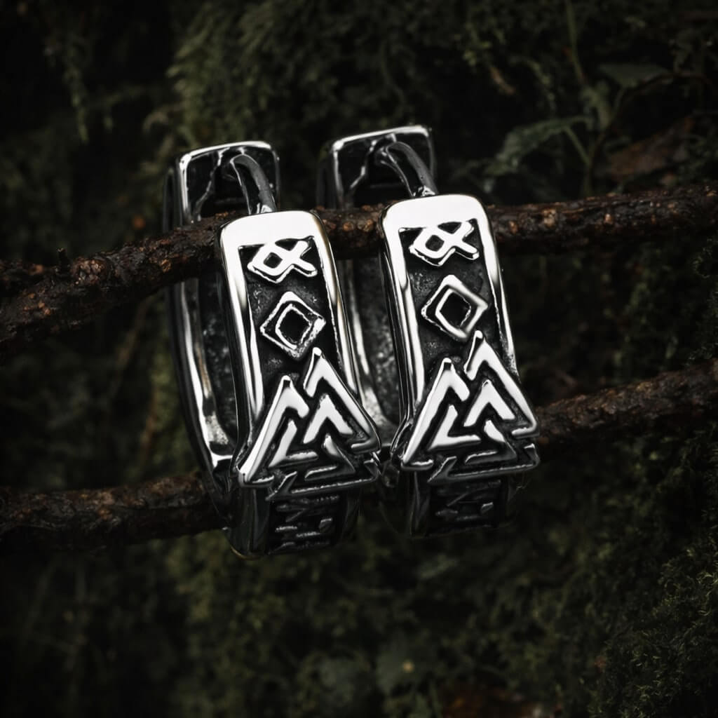 Viking Valknut rune hoop earrings with Norse symbols hang on a branch in a dark forest setting.