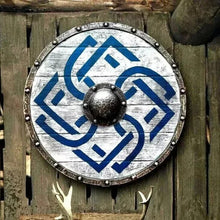 24-inch Viking medieval round shield featuring battle-worn distressed white painted wood with blue interwoven Celtic knot design – weathered steel rim with riveted studs and dark forged iron center boss – rustic wall décor mounted on aged wooden fence with deer antlers below